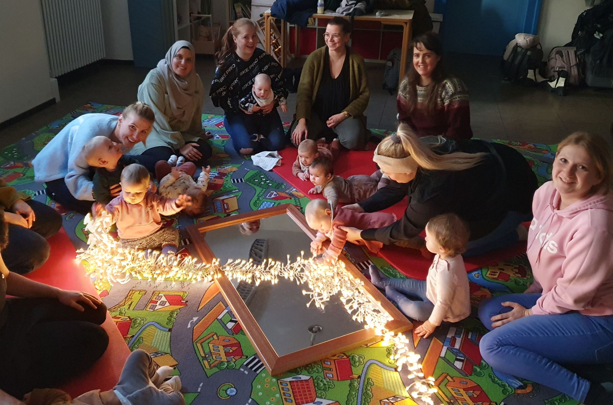 Mütter und Babys sitzen im Kreis um Lichter in einem Gemeindesaal.