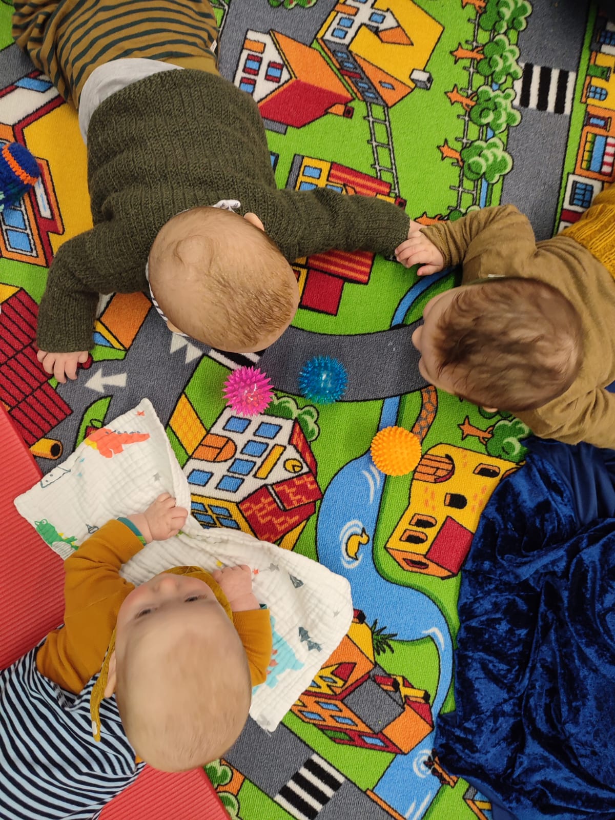 Babys spielen gemeinsam auf einer bunten Spielmatte in der Gemeinde.