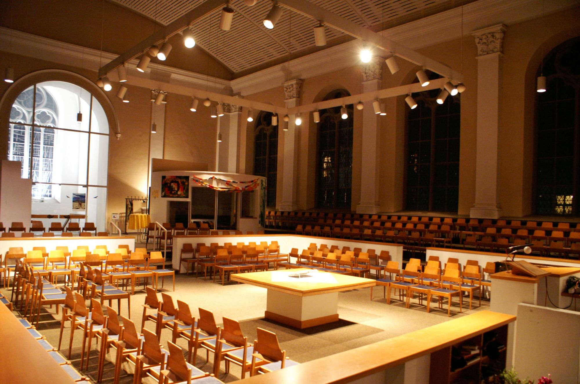 Innenansicht der Sophienkirche mit warmem Licht und modernen Holzstühlen, die quadratisch um einen zentralen Abendmahlstisch angeordnet sind.