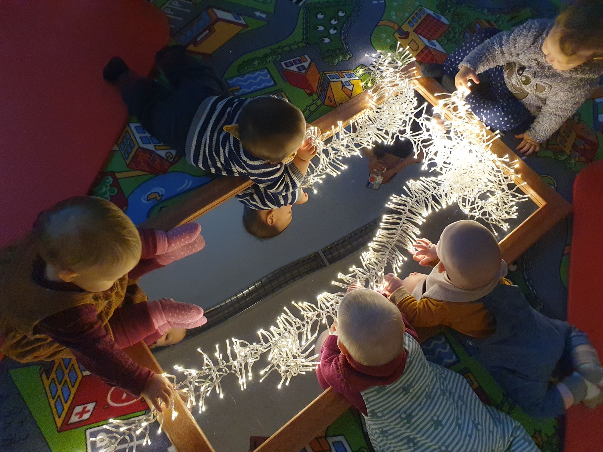 Kleinkinder entdecken eine leuchtende Lichterkette auf einem Spiegel.