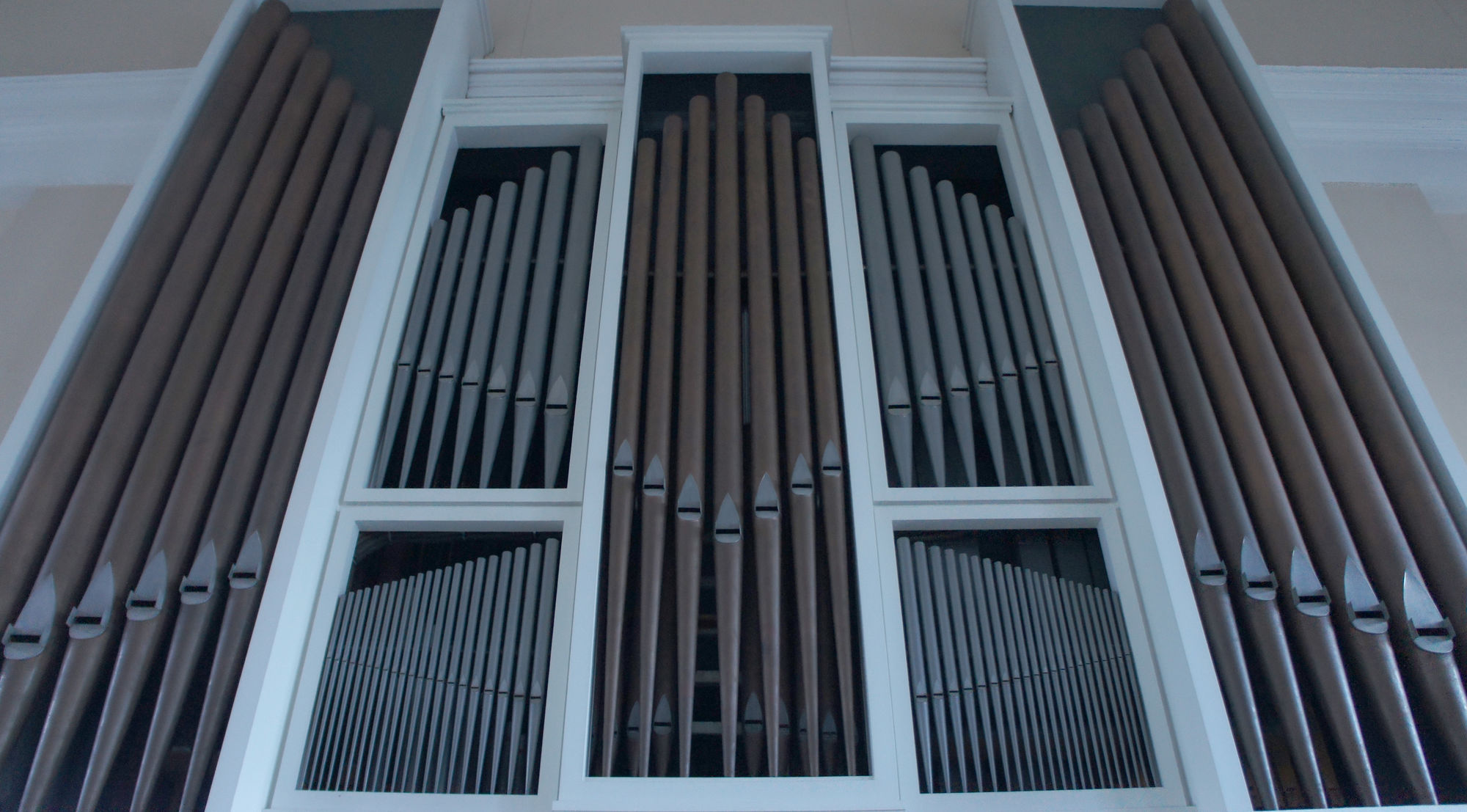 Froschperspektive einer großen Orgel mit silber- und bronzefarbenen Pfeifen in einem weißen, geometrischen Gehäuse.