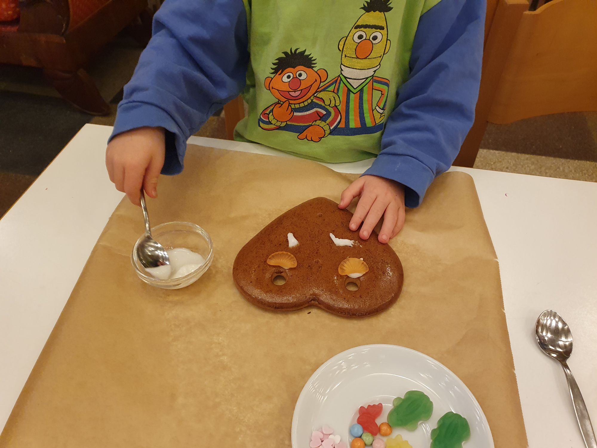 Ein Kind beim Verzieren eines Lebkuchenherzens mit Guss und Süßigkeiten.