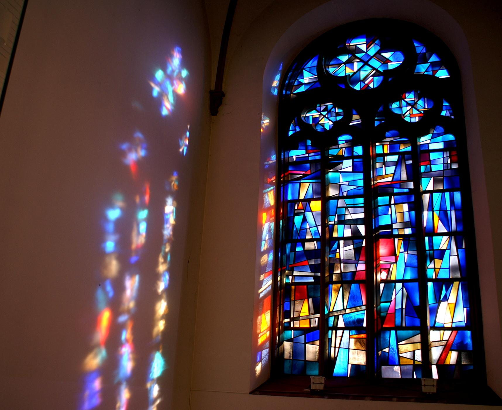 Buntglasfenster mit farbigen Lichtreflexionen an einer Kirchenwand.